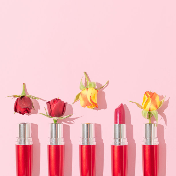 创意布局的黄色和红色盛开的玫瑰花和口红在柔和的粉色背景。简约抽象的时尚化妆概念。复古时尚美容化妆品审美。图片下载