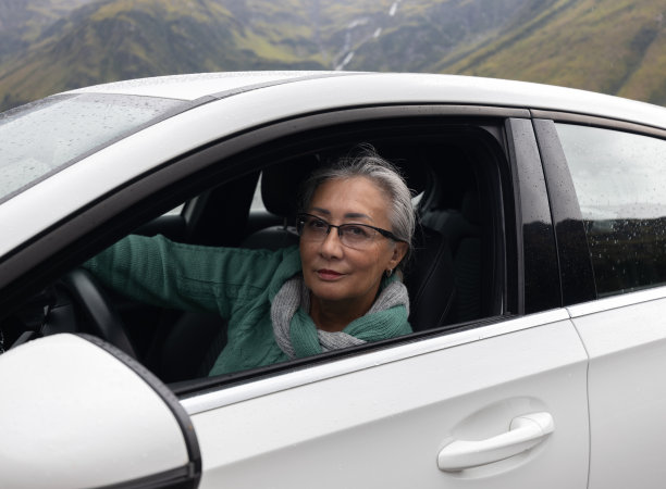 一位头发花白的女士坐在一辆开着窗户的客车的方向盘后面，看着镜头图片下载