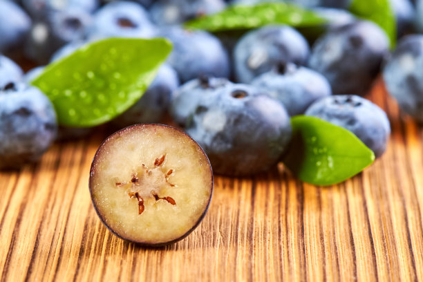 近景的一个切半蓝莓在木表面对蓝莓与绿叶的背景图片下载