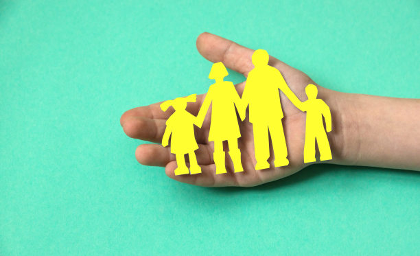 在一个孩子的手中，一个绿色底色的黄色纸剪出的家庭，一个幸福家庭的概念通过一个孩子的眼睛。孤儿院和避难所的概念。有孩子的家庭图片下载