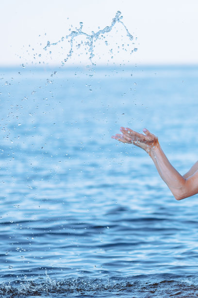 女性的手在海水中溅起清澈的蓝色淡水。蓝色背景上的气泡、水滴、海浪和阳光的反射。图片下载