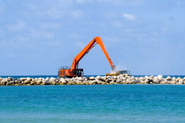 在以色列内坦亚，挖掘机和矿用卡车将石头移入海中，建造防波堤以保护海滩图片下载