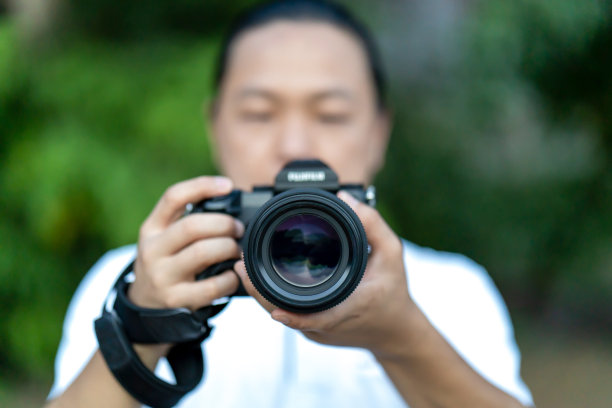 一名亚洲男子手持中画幅相机，对焦拍摄在他面前。图片下载