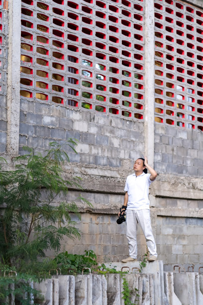 亚洲专业摄影师矫情地站在建筑、混凝土路障上，望向天空，思考如何在聪明的图像中拍摄照片。图片下载