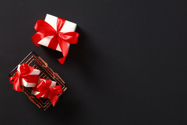 购物篮和白色礼品盒与红色丝带蝴蝶结在黑色背景。黑色星期五打折，促销概念。图片下载