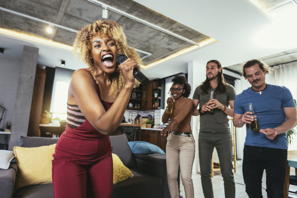 一群多元文化的年轻朋友在家里用麦克风唱歌。图片下载