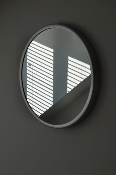 阳光照射下的阴影从百叶帘反射在一面圆墙镜上。优雅抽象的室内设计图片下载