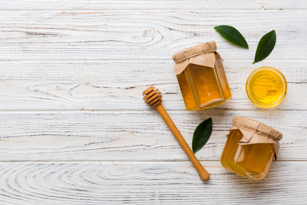 蜂蜜罐与木制蜂蜜勺在白色背景顶部视图与复制空间。美味的蜂蜜瓶图片下载