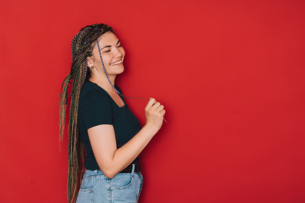 女孩在红色背景下梳着五颜六色的辫子微笑图片下载