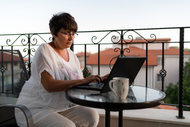 女商人独自坐在阳台上，在她的假期里用笔记本电脑工作图片下载