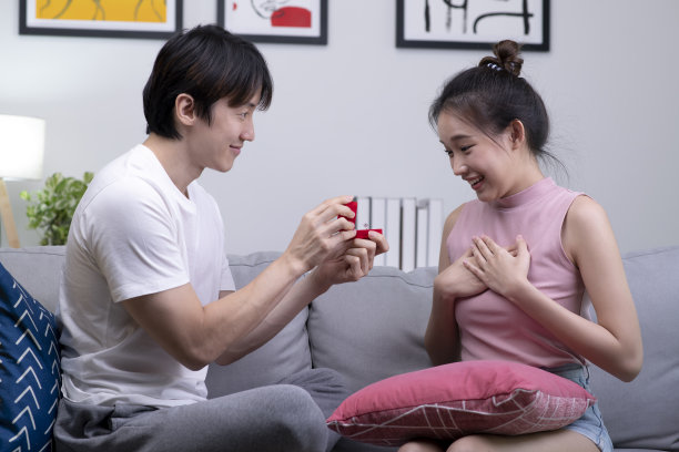 快乐的亚洲男人把装在小红盒子里的订婚戒指送给家里客厅里的女人。图片下载