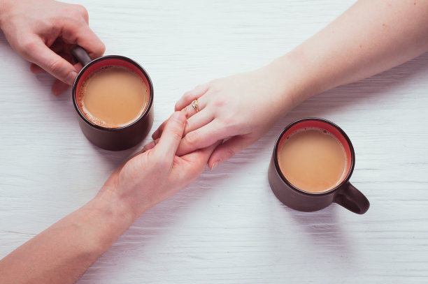 一杯咖啡，一对相爱的情侣在白色的木桌上牵着手。情人节的概念浪漫约会。俯视图，平铺图片下载