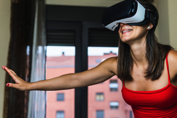 微笑的褐发女子在床上冲浪与她的虚拟现实眼镜。小女孩在她的房间里尝试增强现实，同时有3D体验。图片下载