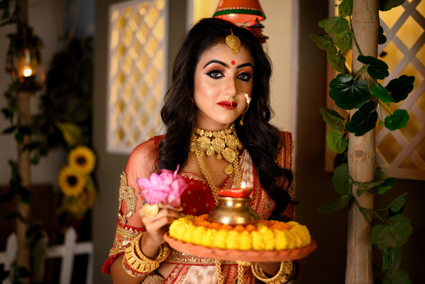漂亮的年轻印度女孩穿着传统的纱丽，黄金珠宝和手镯在工作室照明室内拿着盘子的宗教祭品。印度文化、宗教和时尚。图片下载