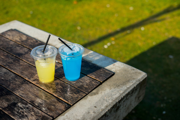透明塑料杯是黄色和蓝色的饮料是在桌子上的户外焦点对前景垂直照片高视角与阴影图片下载