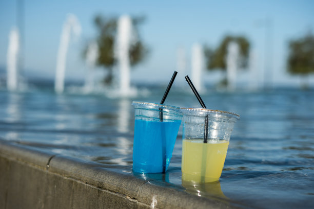 透明塑料杯是在黄色和蓝色的饮料在游泳池在室外焦点的前景水平照片在游泳池狭窄的角度图片下载