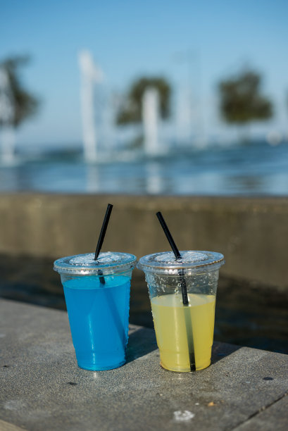 在黄色和蓝色的透明塑料杯饮料是在游泳池在户外焦点的前景垂直照片与水滴在花园狭窄的角度图片下载