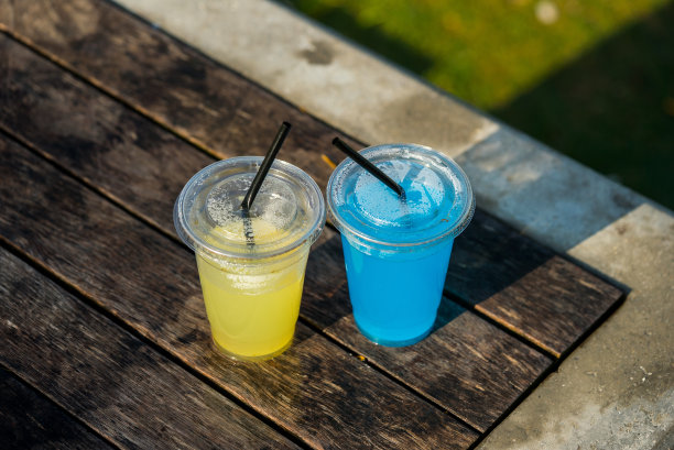 透明塑料杯是黄色和蓝色的饮料是在桌子上的户外焦点在前景垂直照片高点图片下载