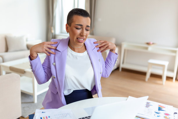 年轻有压力的女人坐在家里的办公桌前的笔记本电脑，触摸疼痛的肩膀与痛苦的表情，在电脑上工作后遭受肩膀疼痛图片下载