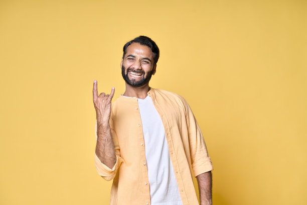 快乐的印度男子展示摇滚手势，在黄色背景中隔离图片下载