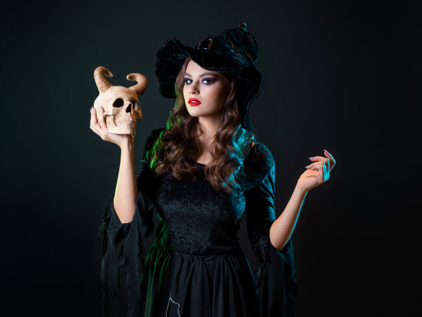 一个年轻美丽的女巫戴着圆锥形的帽子，手里拿着一个恶魔的头骨图片下载