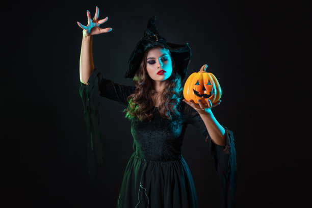 戴着帽子的漂亮女巫在南瓜灯上施咒。图片下载
