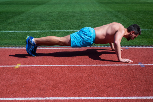 致力于健康。肌肉发达的运动员训练。运动。男性的力量和权力。运动员在板材。运动员做俯卧撑。训练他的核心肌肉。男子在体育场做俯卧撑练习图片下载