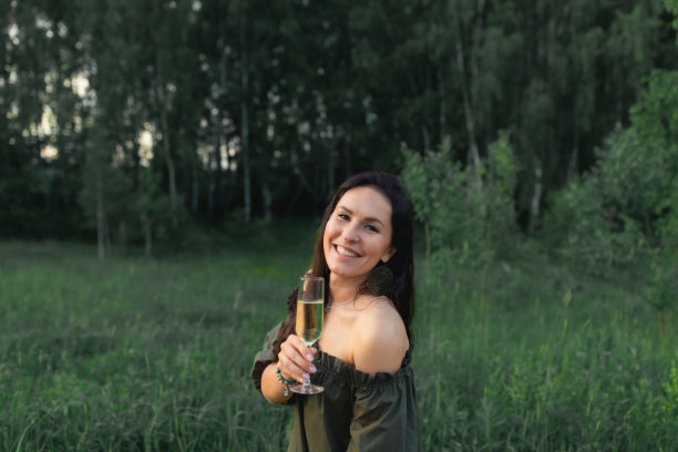 一个迷人的女人拿着一杯香槟酒在大自然的森林里。图片下载