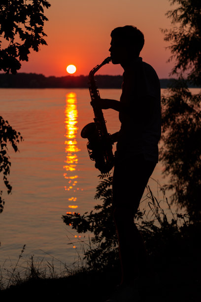一个年轻人的剪影演奏萨克斯在傍晚日落图片下载