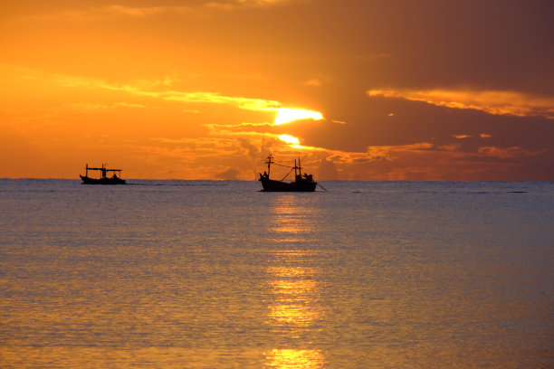 夕阳下，渔船在海面上航行的剪影，金色的光映在水面上，波浪柔和。暑假旅游理念。图片下载