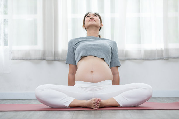 快乐平静孕妇坐在瑜伽垫上伸展热身瑜伽练习，怀孕的年轻妇女享受与瑜伽呼吸和冥想在家里，母亲和健康孕妇概念图片下载