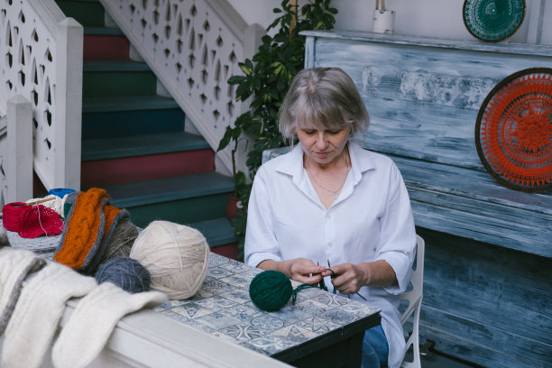 白发苍苍的美丽成年女子坐在家里，桌上放着针织针和羊毛图片下载