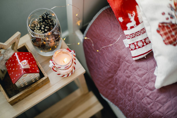 节日装饰。燃烧的蜡烛，陶瓷的房子，坛子上的木锥在床头柜上图片下载