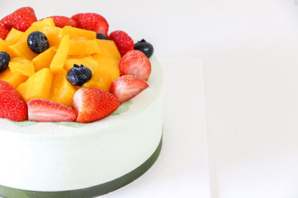 奶油生日蛋糕，水果蛋糕，上面有新鲜的草莓，蓝莓和芒果，放在框架和白色桌子的左边图片下载