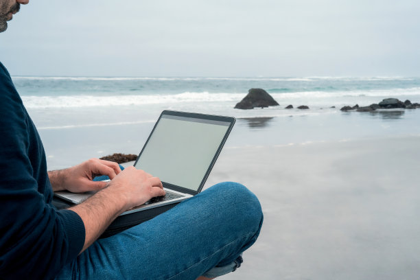 未知男子坐在沙滩上轻松的笔记本电脑工作，双手观看图片下载