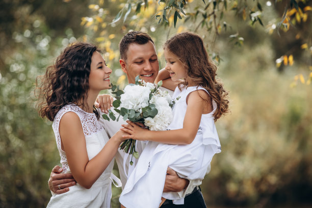 家庭的母亲，父亲和女儿是美丽和快乐的一起在假日，穿着白色的衣服，拿着花束，在大自然图片下载