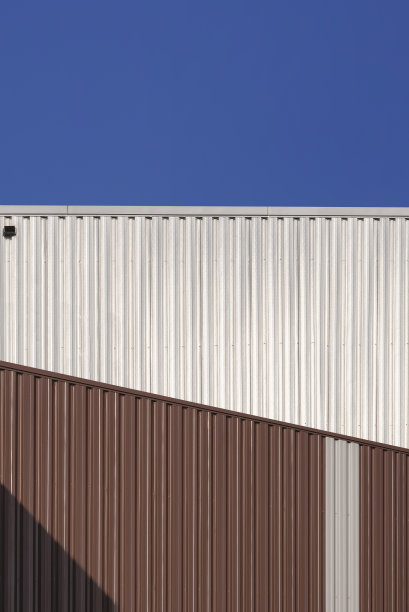 2栋棕色和银色的波纹钢仓库，衬着蓝色晴空的垂直框架图片下载