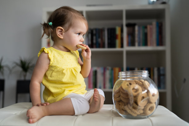 一个女婴坐在家里，吃着玻璃罐里的饼干图片下载