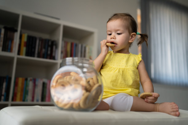 一个女婴坐在家里，吃着玻璃罐里的饼干图片下载