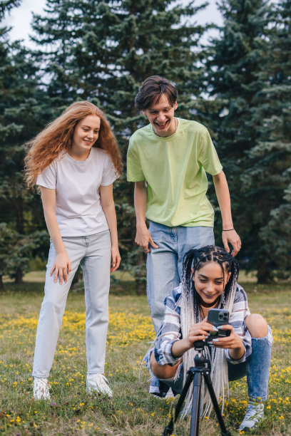 千禧一代的青少年站在公园里为他们的网络频道拍摄视频。智能手机的现代技术和配件。舒适和方便。图片下载