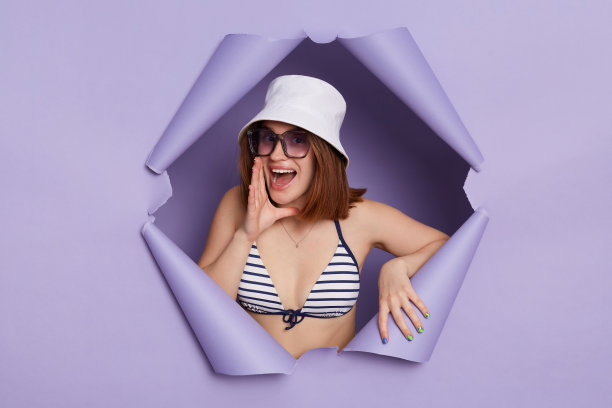 画像高兴的女人穿着条纹泳衣摆姿势在撕裂的紫色纸墙，站着大声尖叫，宣布，看着相机。图片下载
