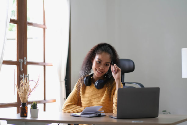 年轻的快乐微笑的西班牙亚裔学生戴着耳机在网上聊天会议使用笔记本电脑在大学校园或虚拟办公室。女大学生远程学习。图片下载