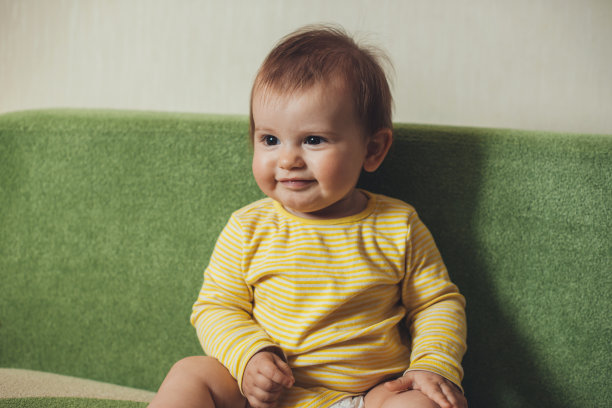 快乐的白人小女孩穿着黄色的衣服，坐在家里的绿色沙发上，望向远方，微笑着。家庭护理。微笑快乐的孩子。婴儿护理。亲子关系的概念。图片下载