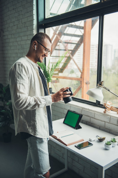 戴眼镜的男子正在看他刚刚用相机拍下的照片。时尚的照片站在室内，伟大的设计为任何目的。图片下载