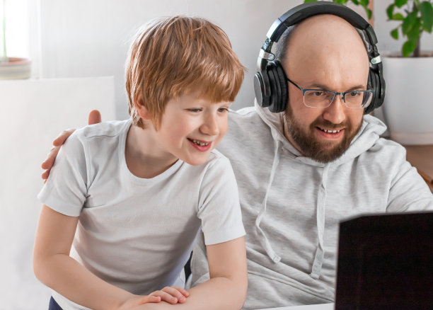 爸爸和儿子笑着玩视频聊天，看着笔记本电脑的屏幕图片下载