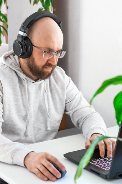 千禧一代的光头男，戴着眼镜和耳机，看着屏幕，在家里的笔记本电脑上远程工作，远程进行商务谈判图片下载