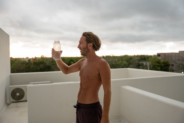 早上锻炼后，年轻人在屋顶上从可重复使用的水瓶里喝水图片下载