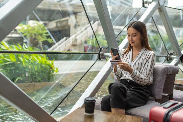 年轻聪明的亚洲女商人看着她的信用卡详细信息，同时通过她的智能手机在一个随机的咖啡馆进行在线支付图片下载
