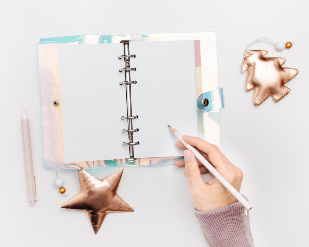 女人写在开螺旋笔记本或日记与彩色梯度颜色覆盖白色，闪亮的圣诞装饰，空白页。规划个人未来目标和新年想法的概念图片下载