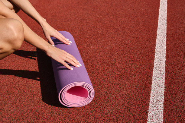 特写一个女人的手卷起一个运动垫，准备上瑜伽课。健身瑜伽户外锻炼图片下载